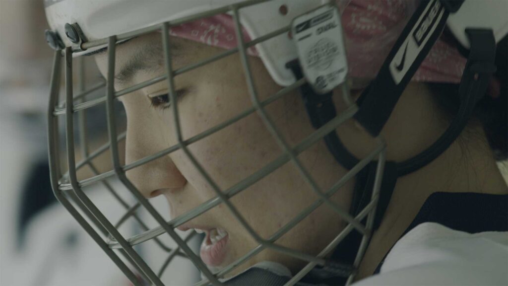 Close-up of Choa’s face, a female Korean ice hockey player, focused and ready to step onto the ice during a game as the only woman on South Korea’s men’s team.