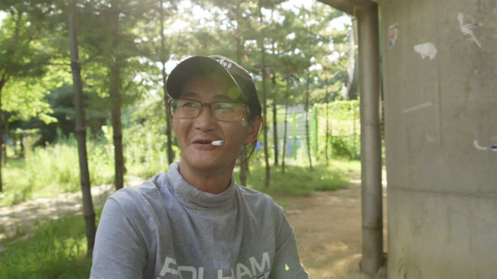 A screenshot from the Varúð music video by Icelandic band Sigur Rós, depicting a homeless man smoking on a bench near Yongsan Station in Seoul, South Korea