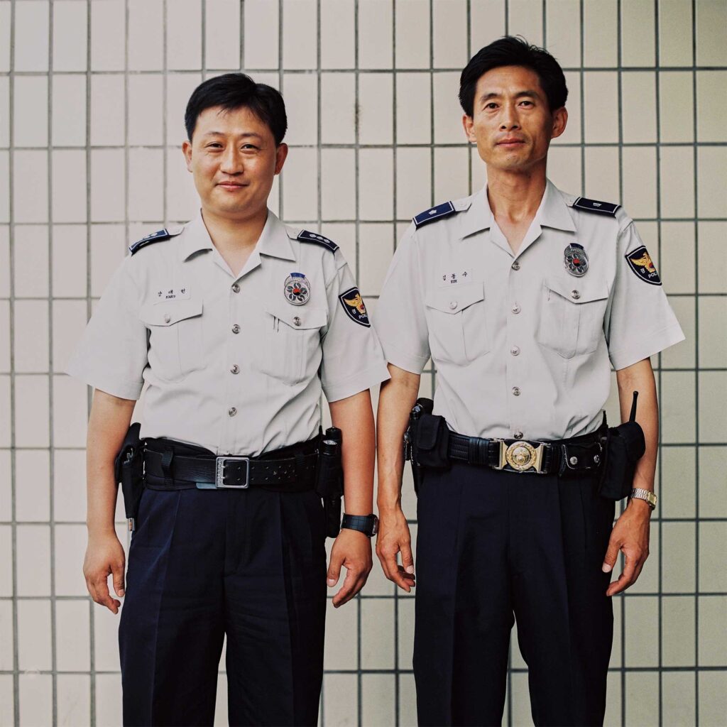 Identically dressed police officers stand before a tiled wall in Seoul, South Korea