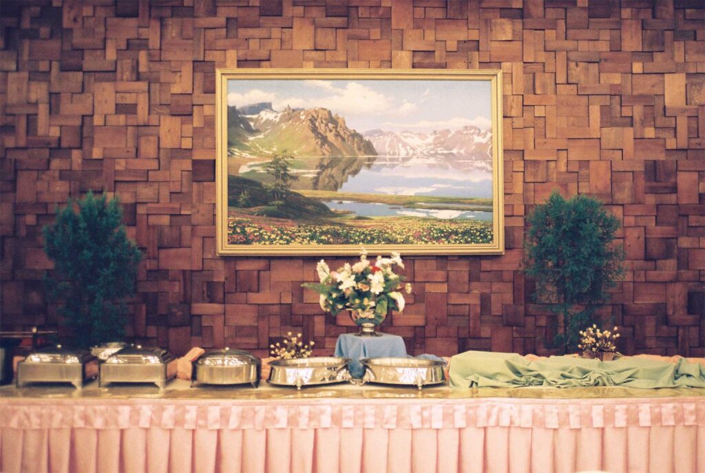 Mountain landscape painting from North Korea adorning a dining hall, hung above a table against the wall for catering.
