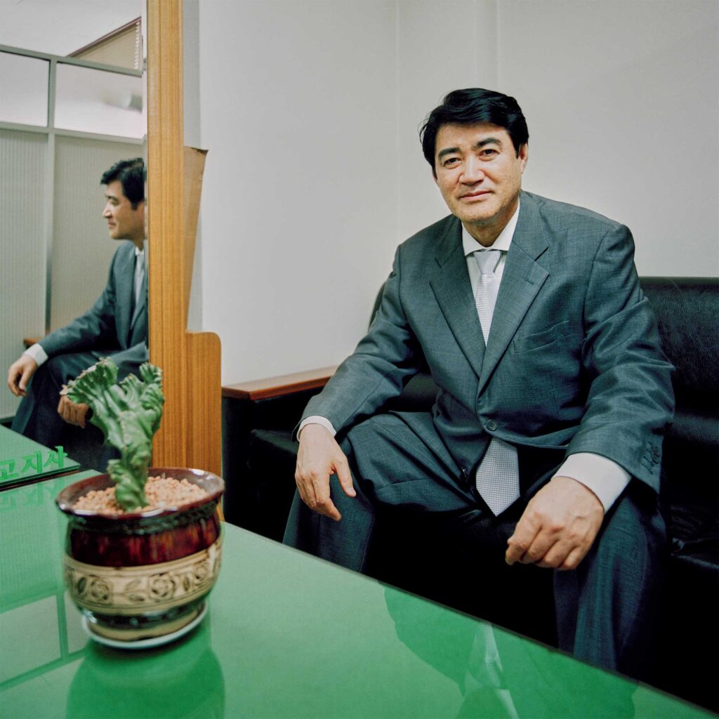 A Korean man in an oversized suit sits in an armchair in an office meeting area in Seoul, South Korea