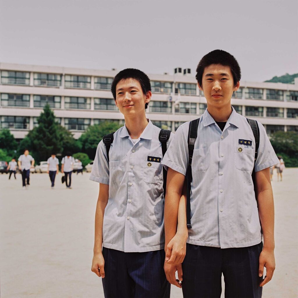 Identically dressed male high school students stand on the sports playground of their school in Seoul, South Korea, with entangled arms