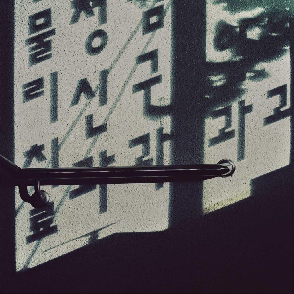 Korean letters reflected on a wall in a Seoul building staircase at night, illuminated by lantern light