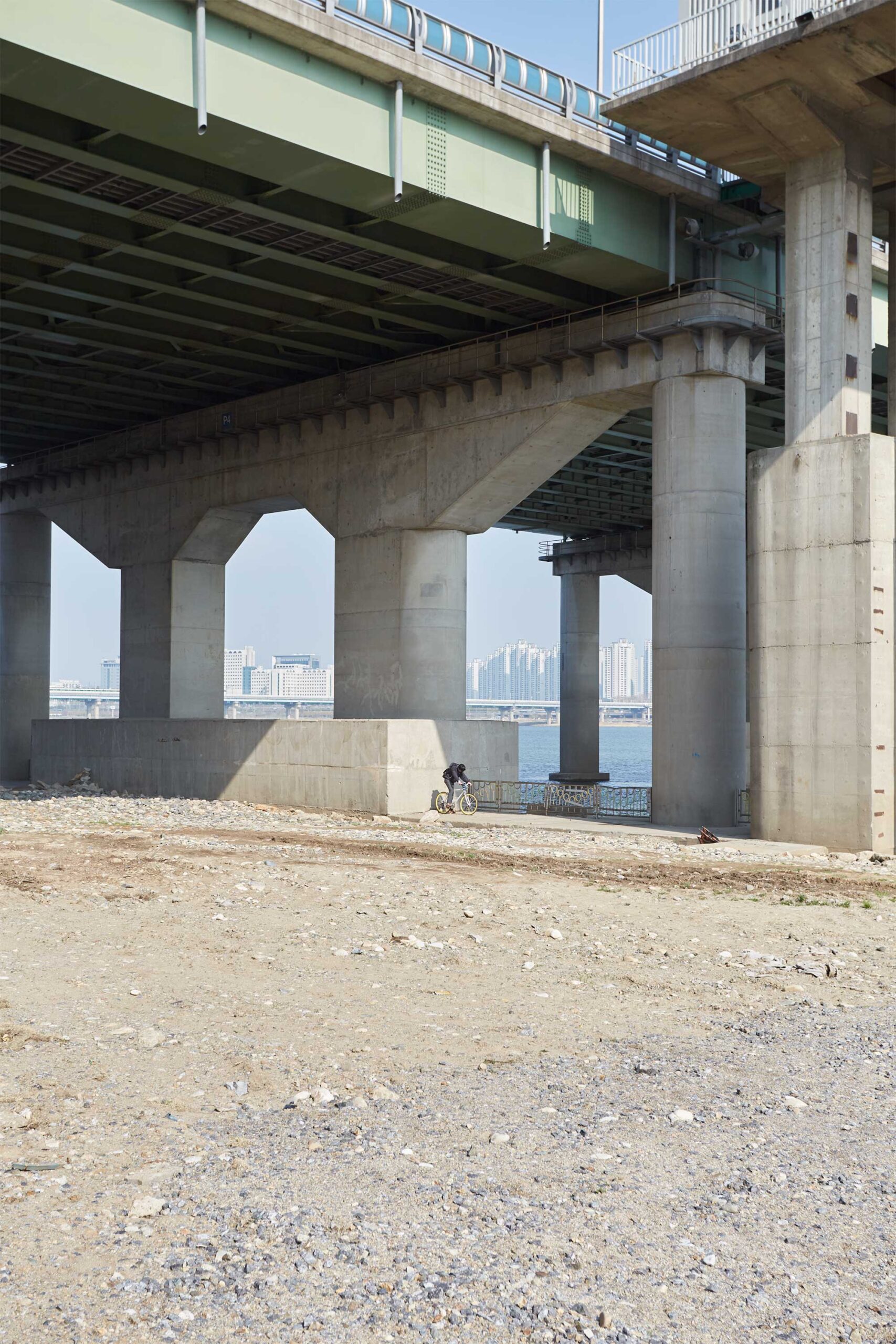 A solitary cyclist rides beneath a bridge spanning the Han River in Seoul, South Korea