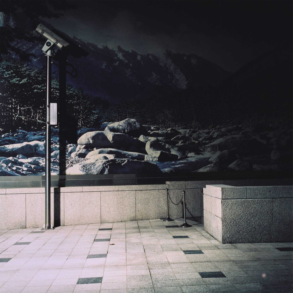 A nighttime mural on a building corner in Seoul, South Korea, featuring large rocks in a mountain stream bed. A CCTV camera is positioned in front of the mural