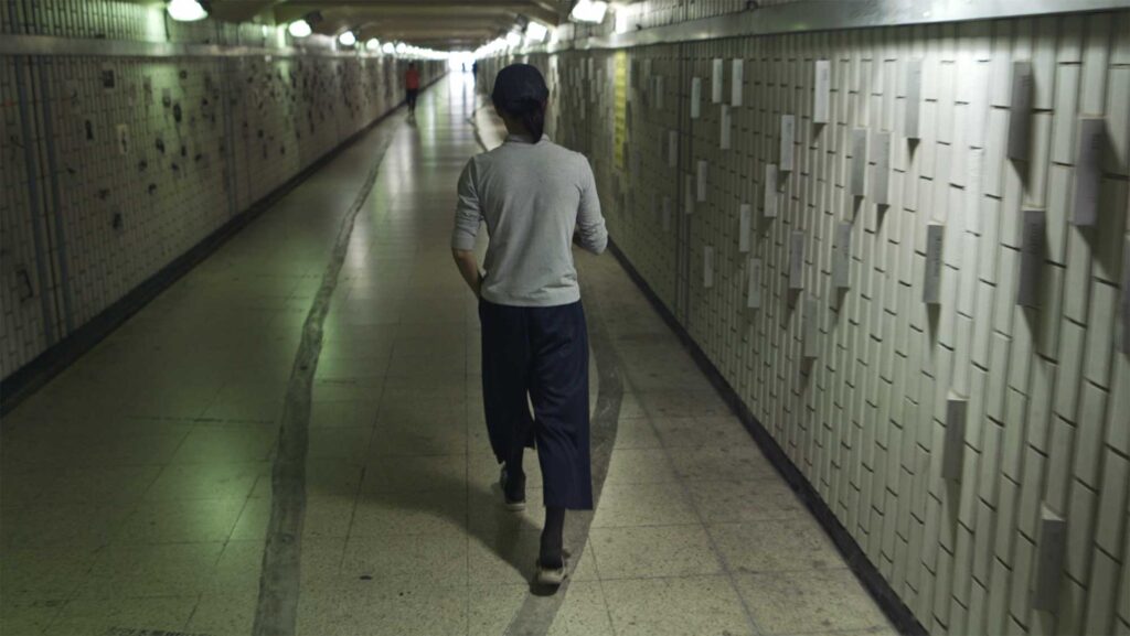 A screenshot from the Varúð music video by Icelandic band Sigur Rós, showing a homeless man walking through a pedestrian underground pathway in Seoul, South Korea
