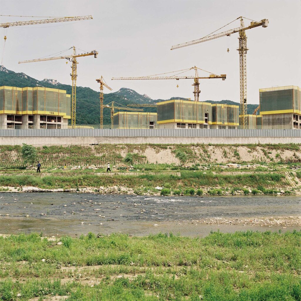 A stream flows towards the majestic Han River, framed by the construction site of high-rise apartment buildings rising in the background