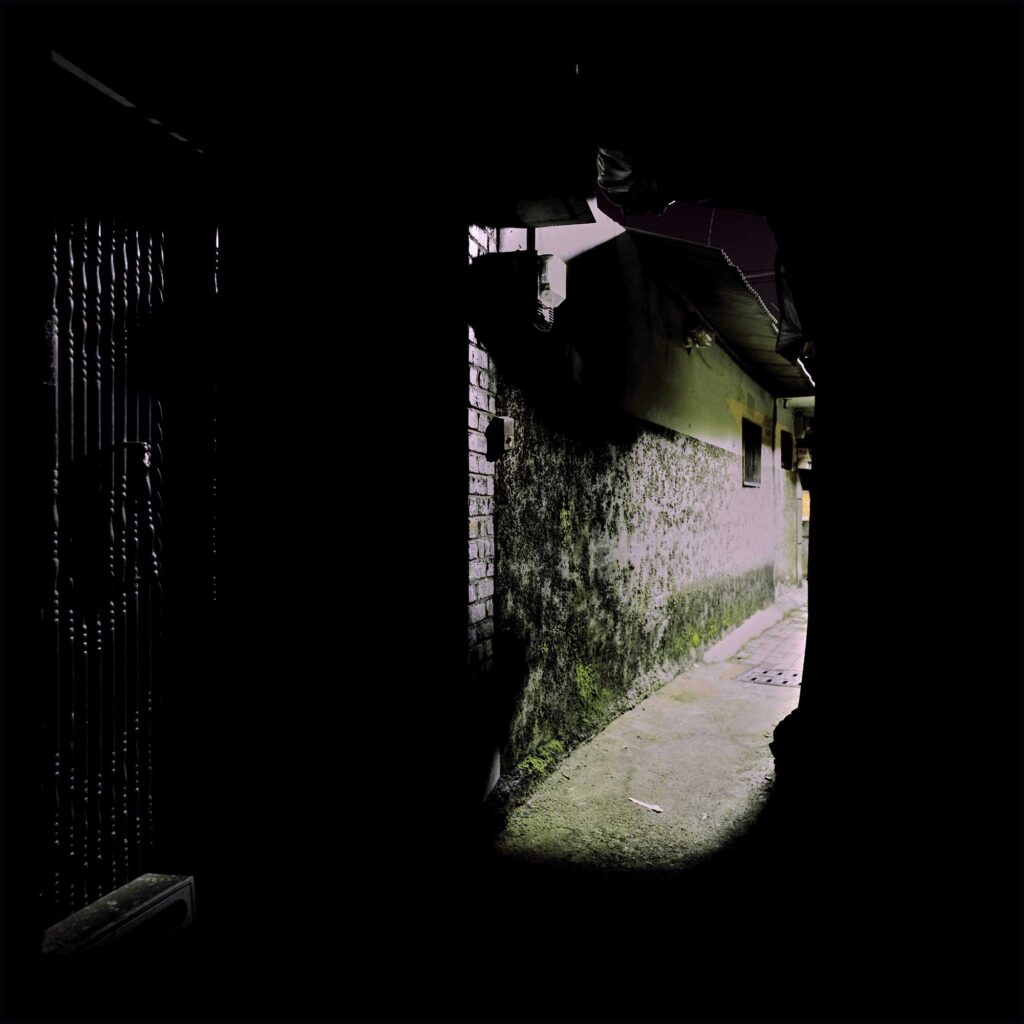 At night, a dark alley in the Korean countryside with a street lantern casting light at the end