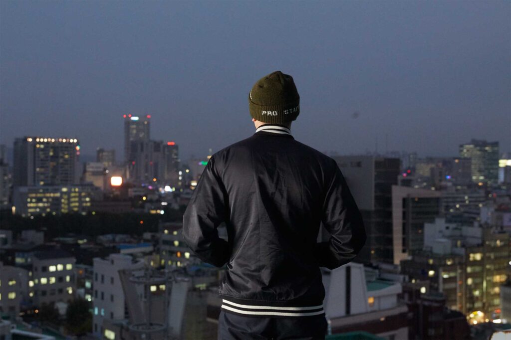 DJ Soulscape (Min Jun Park) stands on a rooftop, gazing over Seoul, South Korea, at night