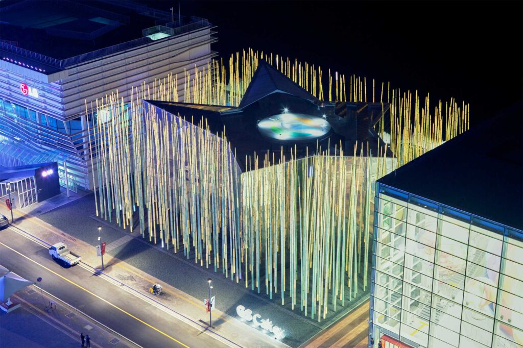 The GS Caltex building in South Korea, with its distinctive yellow and green LED blades, casts mesmerizing reflections on its mirrored surface, showcasing its iconic star-shaped core adorned with the GS Caltex logo