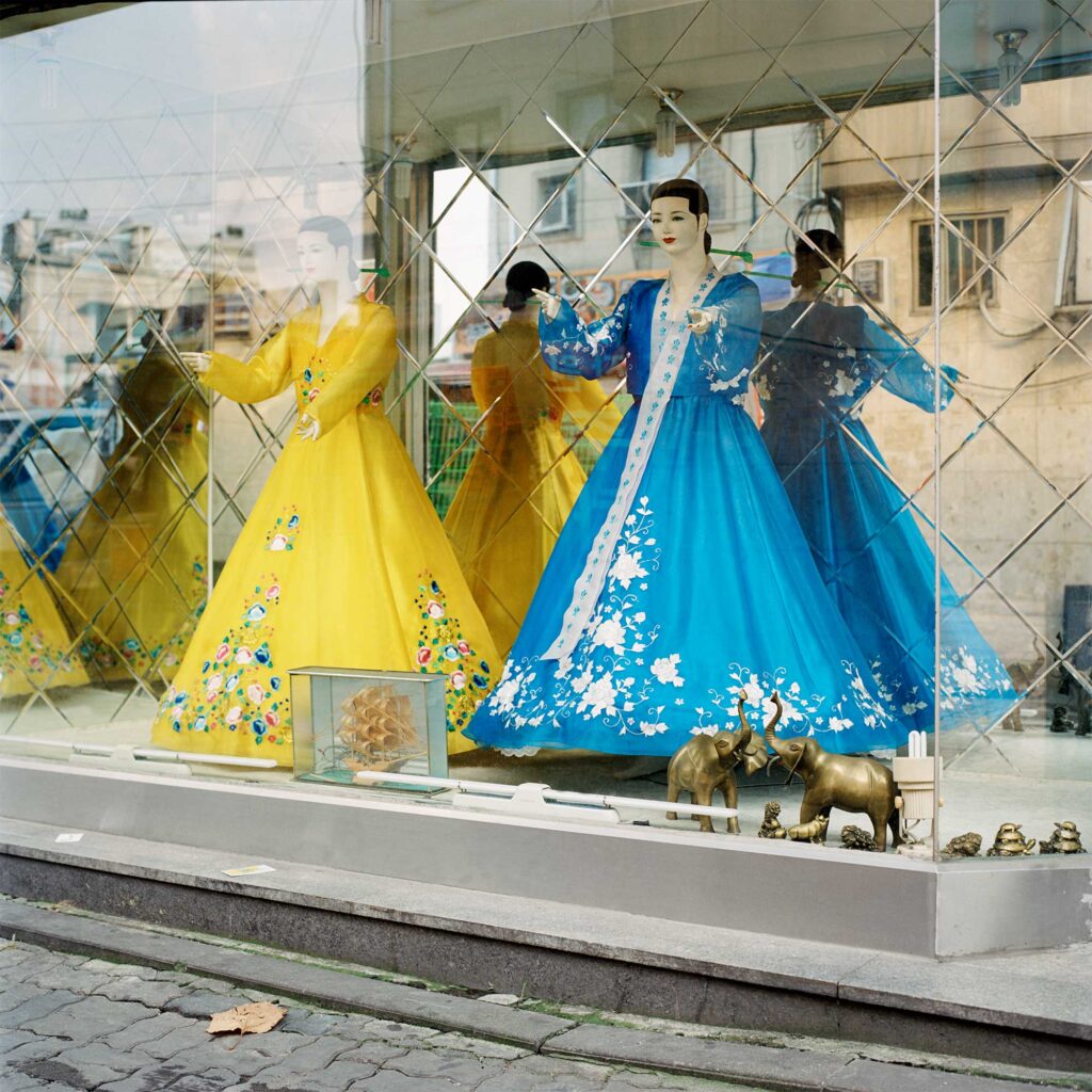 In Jongro, Seoul, South Korea, two mannequins elegantly dressed in traditional attire grace a shop window, reflecting the bustling cityscape towering above