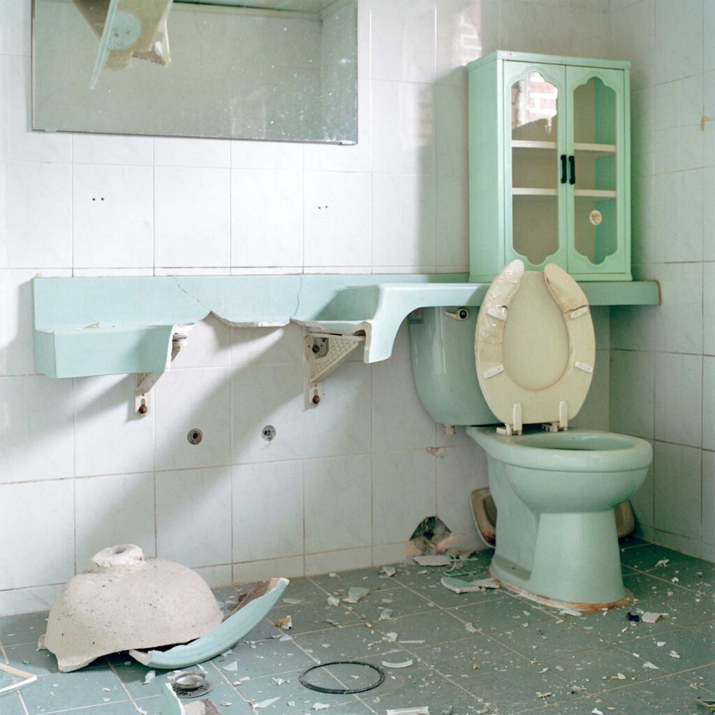 A demolished mint-colored bathroom in an abandoned home in Seoul, South Korea, with the washing basin smashed and lying on the ground