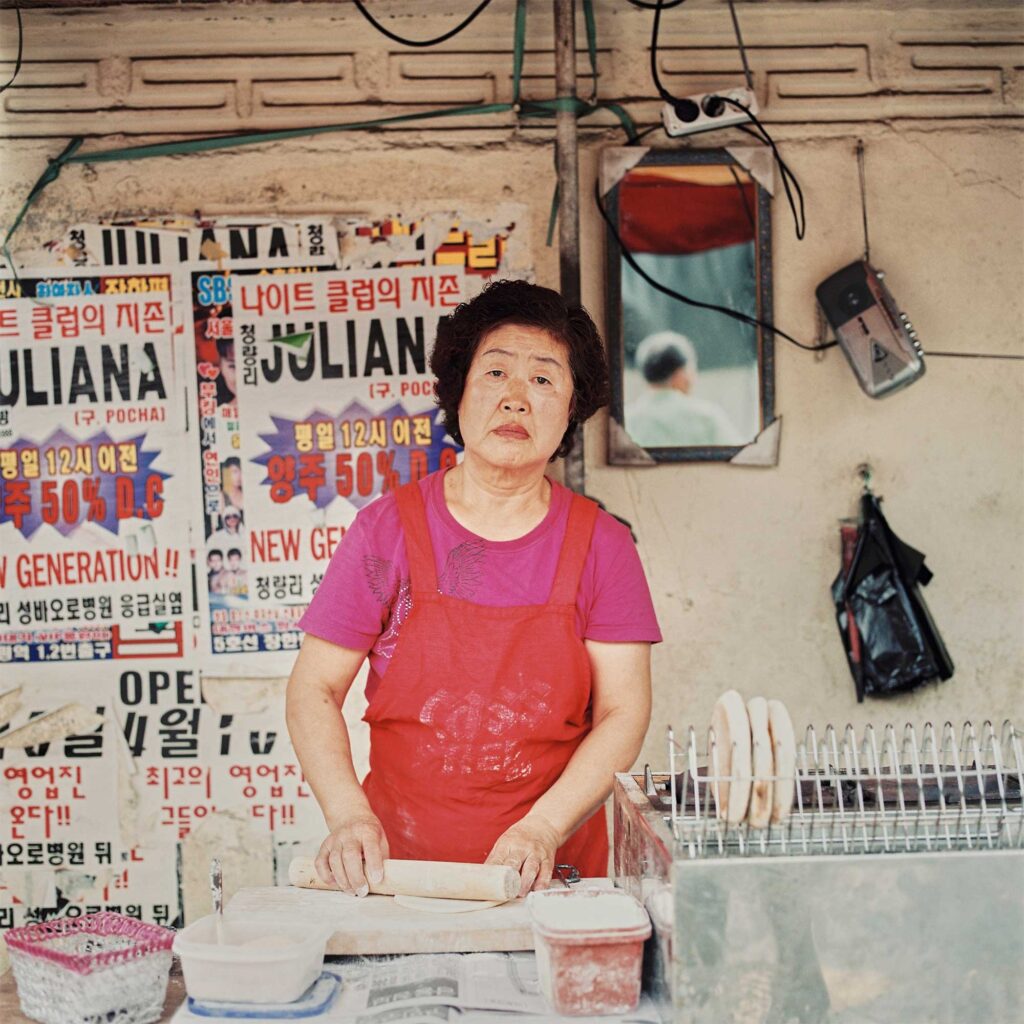 A portrait of an elderly Korean street vendor selling sweet baked goods at a corner intersection in Seoul, South Korea