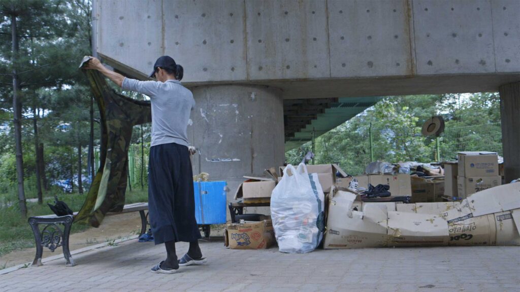 A screenshot from the Varúð music video by Icelandic band Sigur Rós, depicting a homeless man organizing his belongings in a small park near Yongsan Station in Seoul, South Korea, where he, among other homeless people, camps out
