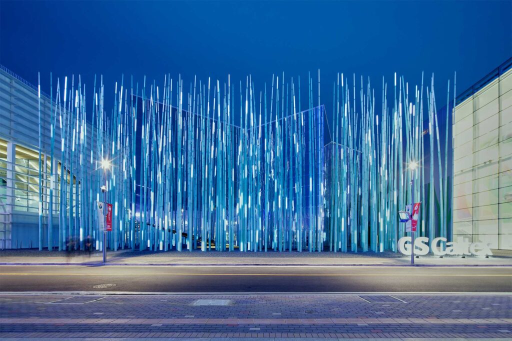 The facade of the GS Caltex building in South Korea is adorned with green and blue LED blades, casting reflections on its mirrored surface