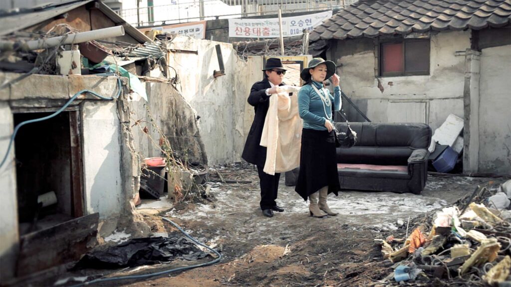 A scene from Röyksopp's 'Senior Living' music video: An elderly couple dresses up in fancy attire against the backdrop of a construction site in Seoul, South Korea.