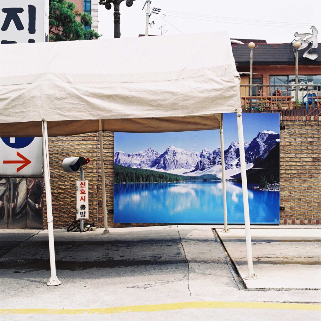 A covered passage at a car wash center in Seoul, South Korea. The backdrop wall features a large photo of a serene snowy mountain landscape by a beautiful blue lake