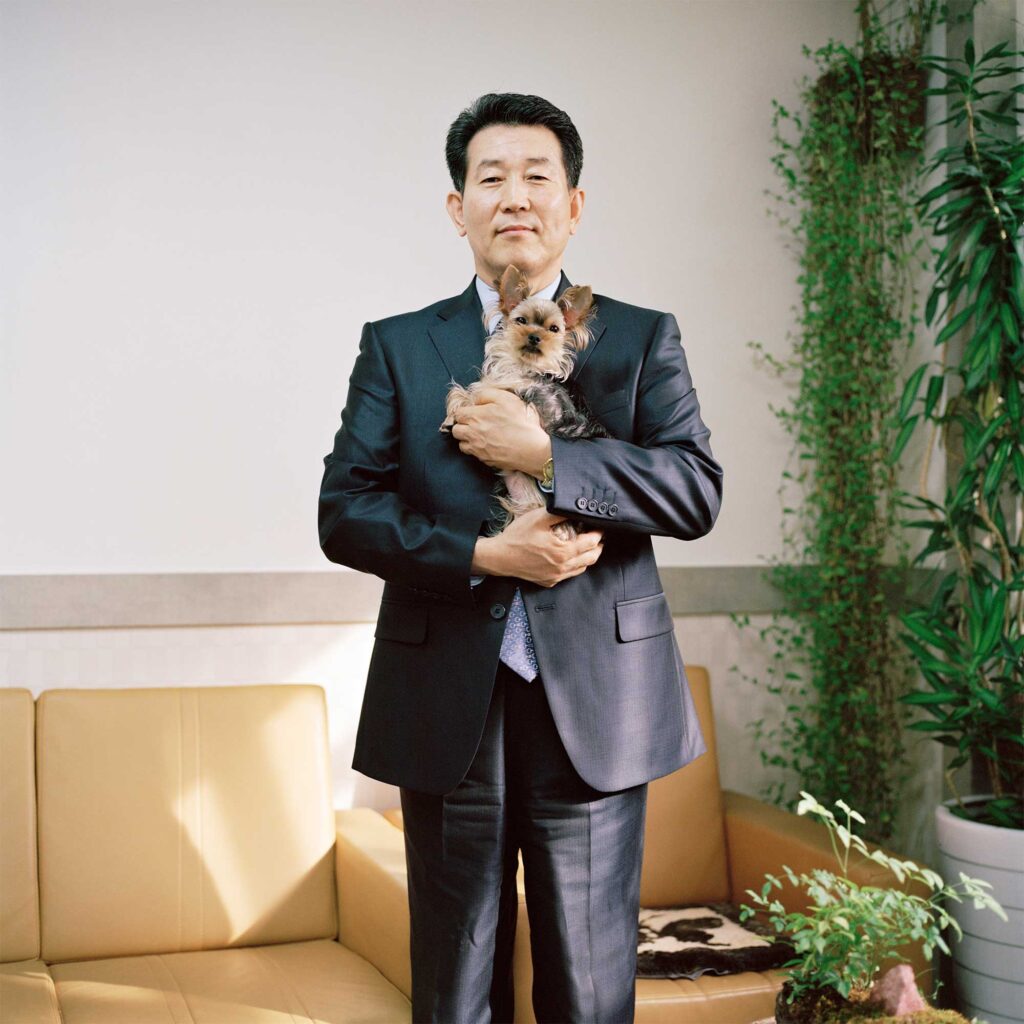 A portrait of a South Korean priest holding his small dog in his arms. This priest plays a vital role in assisting North Korean defectors to resettle in South Korea