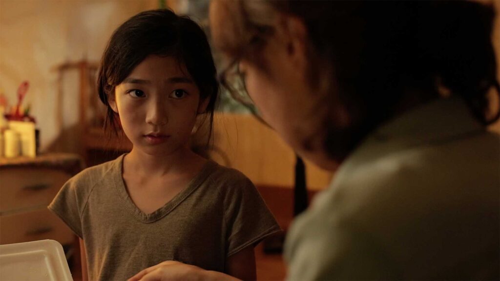 A young girl in the short film "Cold Summer" in her scabby home with a stranger woman in a run-down neighborhood in Seoul, South Korea