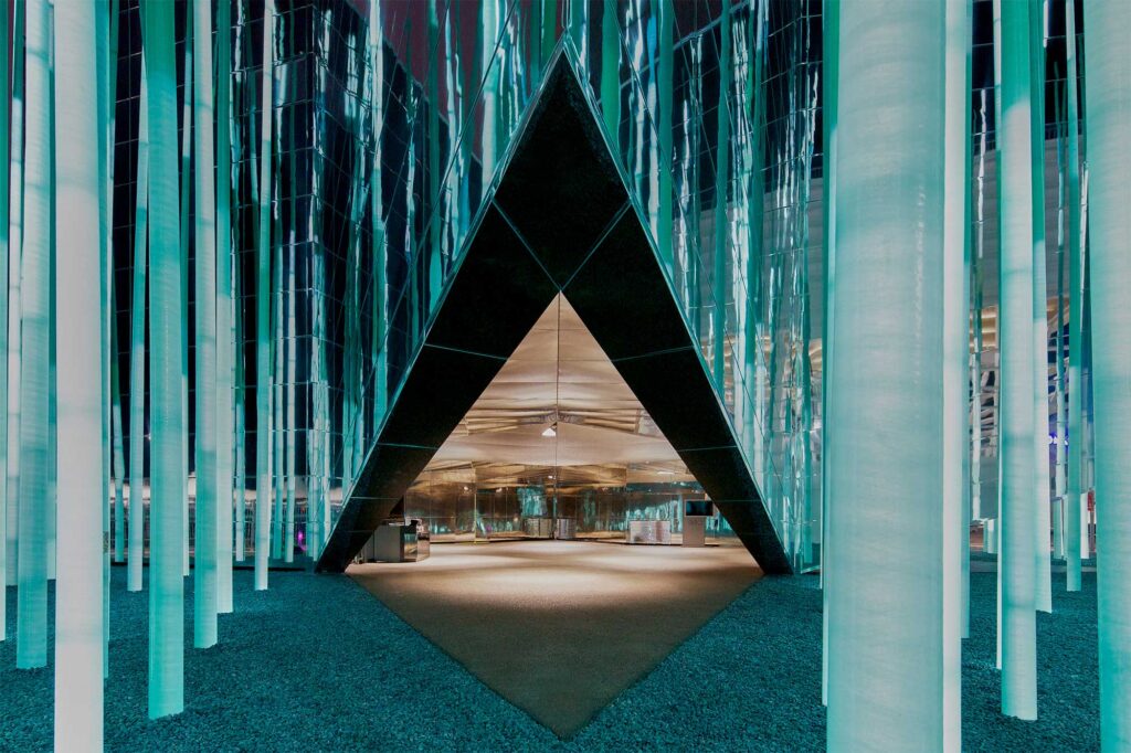 At night, the entrance of GS Caltex building illuminates with green LED-lit blades reflecting on its mirrored facade, while warm lights brighten the interior entrance area