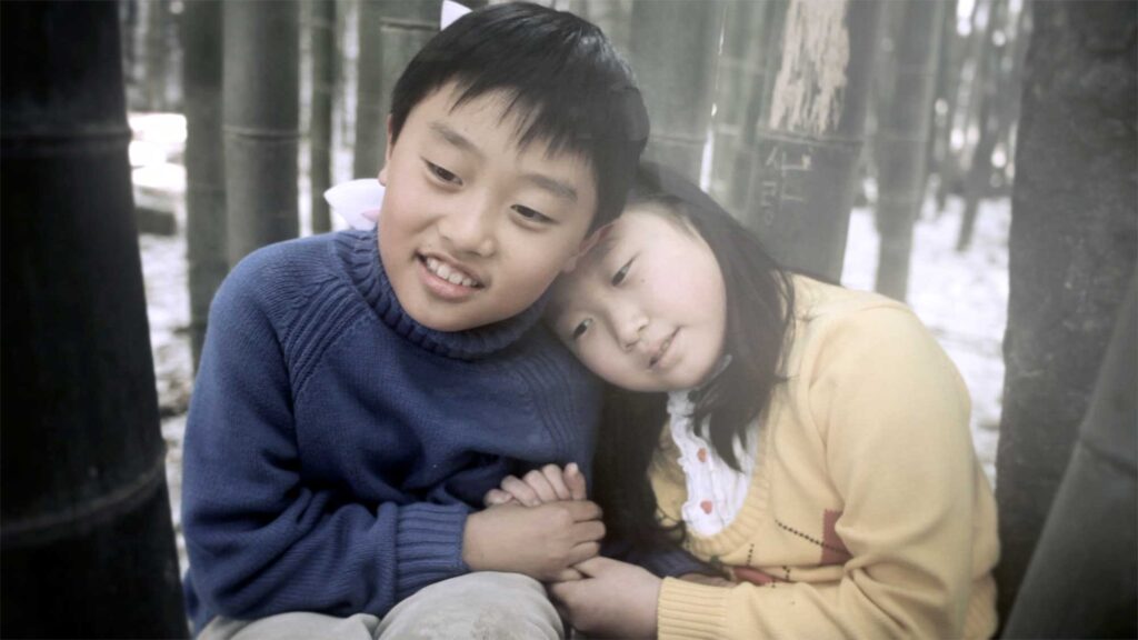 A scene from the Wolf + Lamb vs. Soul Clap 'Lonely C' music video: In a remote South Korean countryside village, the sister and brother, depicted as young children, crouch down in a bamboo forest, holding hands