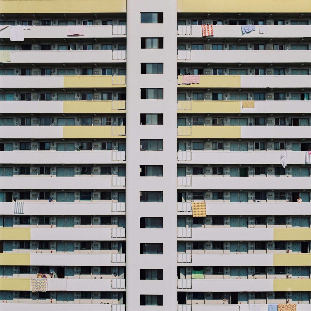 Structured apartment building facade with colorful blankets draped over balconies, breaking the symmetrical pattern