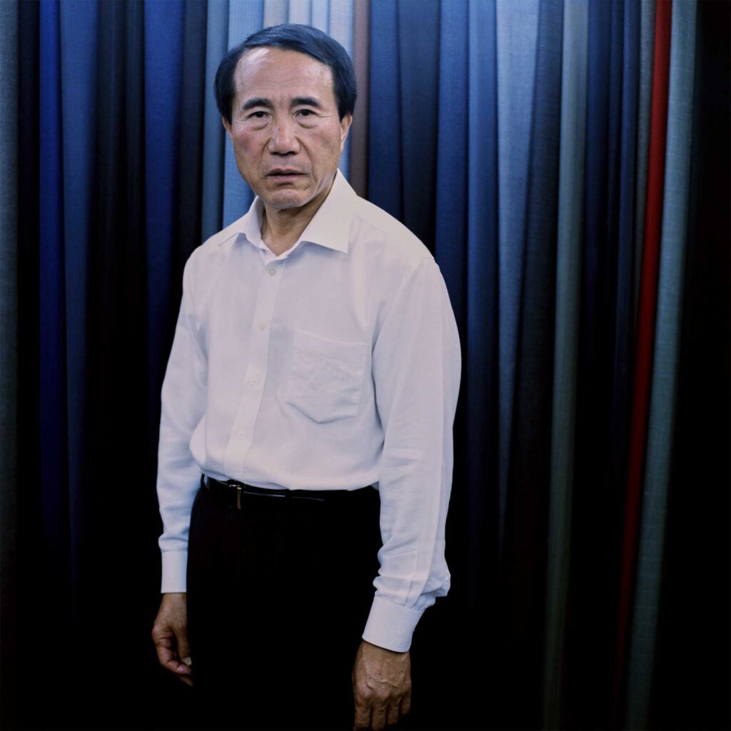 Suit tailor in Itaewon, Seoul. Surrounded by colorful fabrics, he wears a white dress shirt and black pants