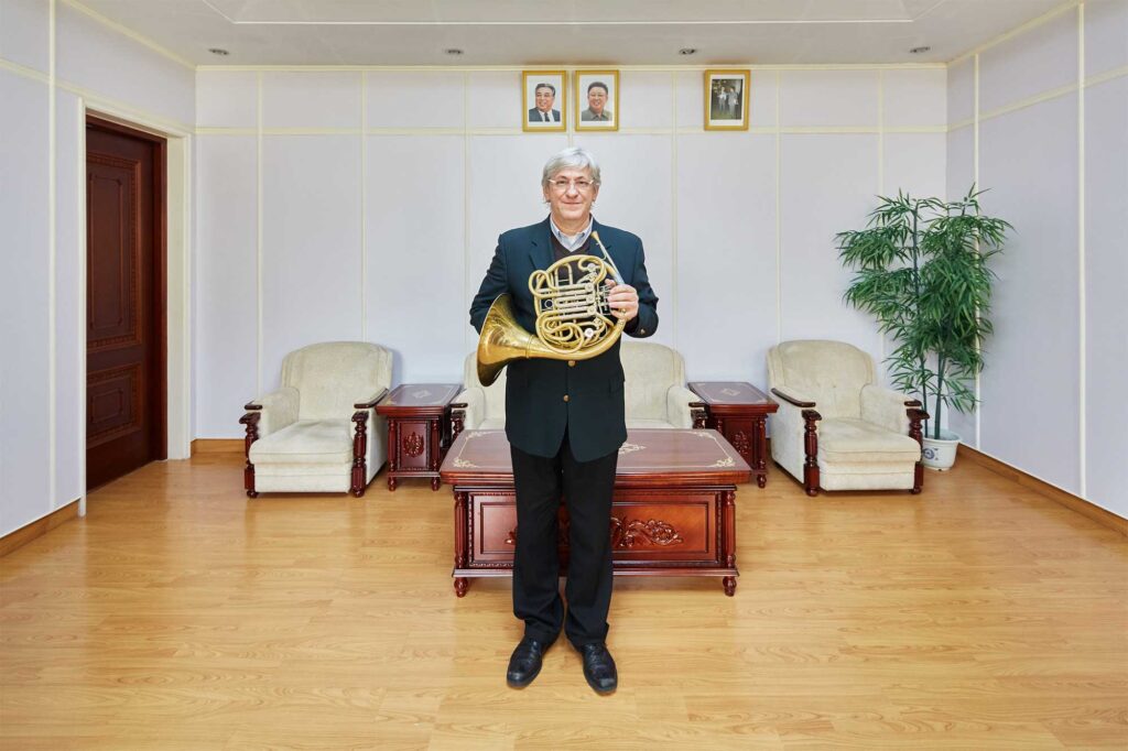 Munich Chamber Orchestra tubist in Pyongyang, North Korea, with portraits of North Korean leaders Kim Il-Sung and Kim Jong-Il on the wall