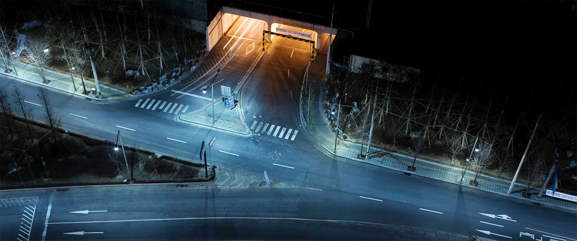 Street intersection leading to tunnel at night, blending yellow tunnel light with blue night ambiance
