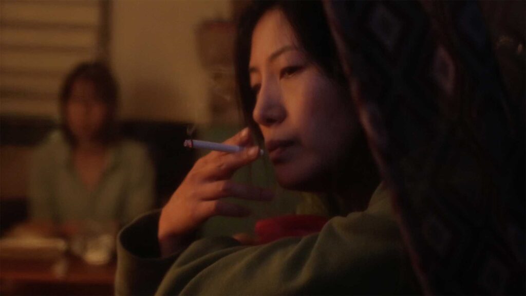 The suicidal mother of a young girl in the short film "Cold Summer" having a smoke in a tiny, scabby home, sitting next to the window in a run-down neighborhood in Seoul, South Korea