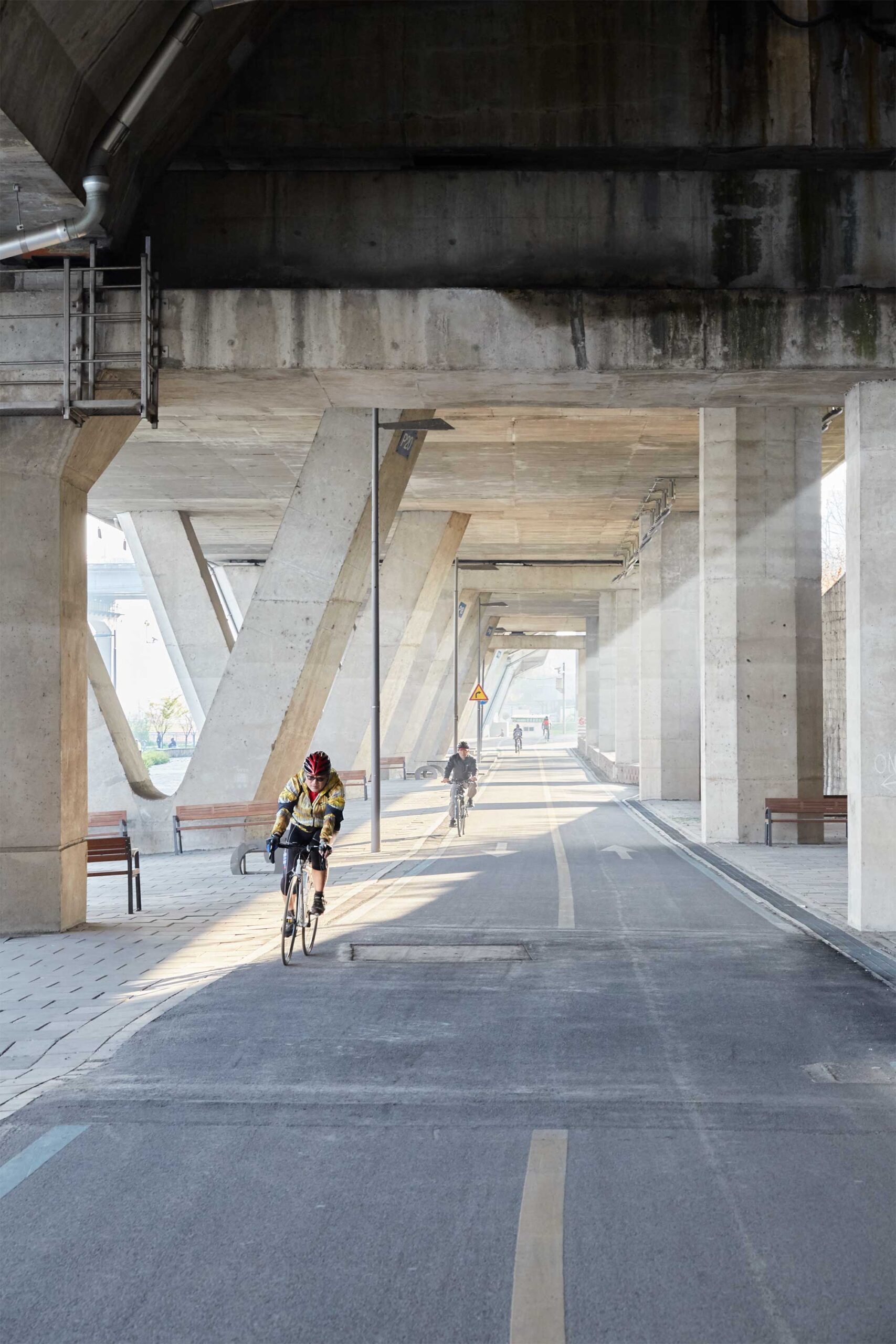 Two cyclists ride on the bike path under a highway flyover beside the Han River in Seoul, South Korea