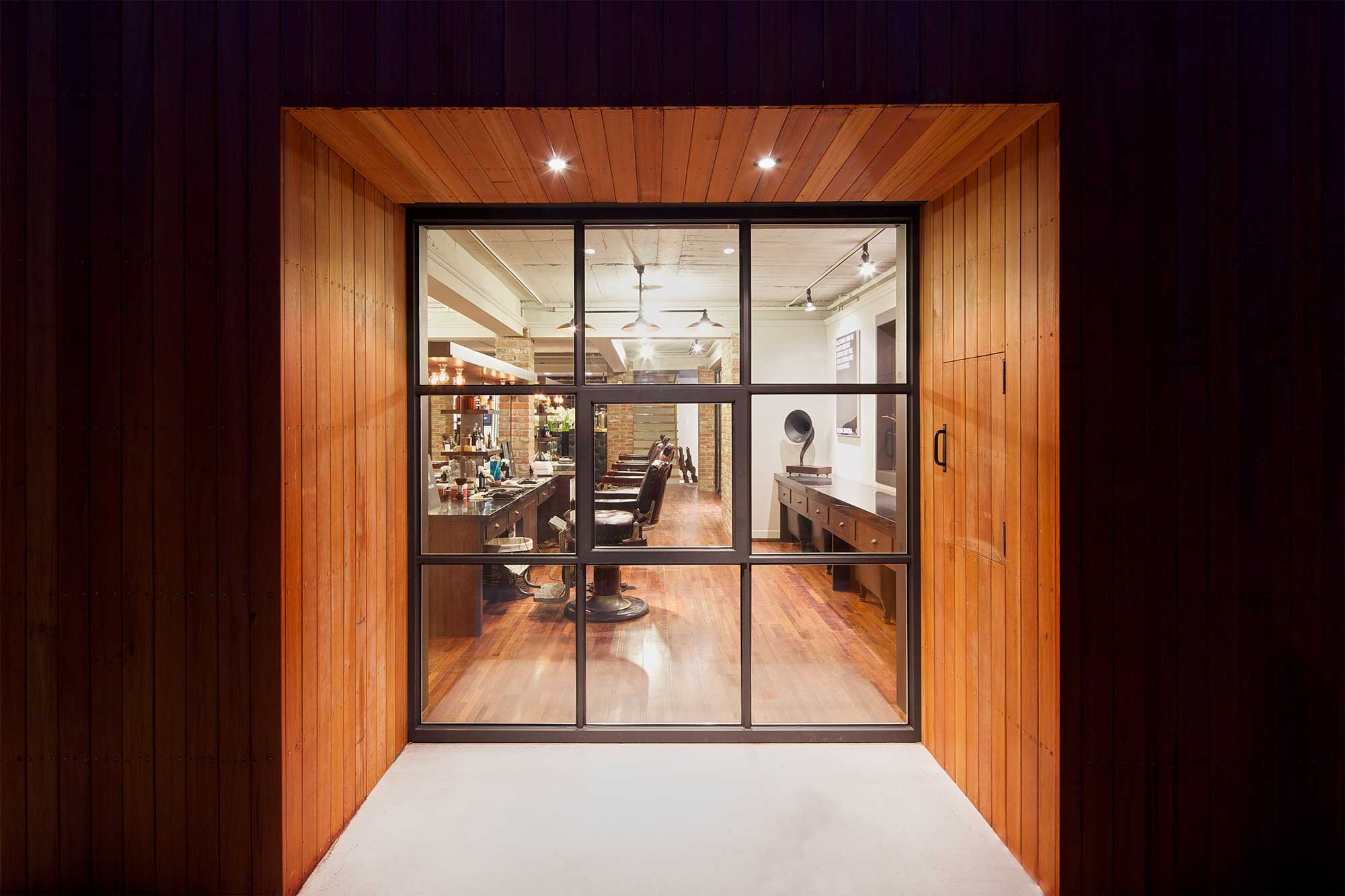 View from outside into the interior of the gentlemen's barber shop HERR in Seoul, South Korea, featuring vintage barber chairs in a row and an array of grooming tools spread across the counter.