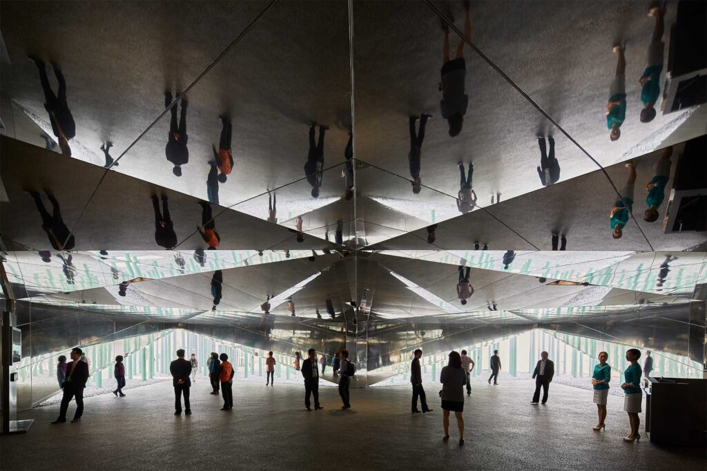 During the day, people move within the interior entrance area of the GS Caltex building, their reflections multiplying on the mirrored ceiling surface