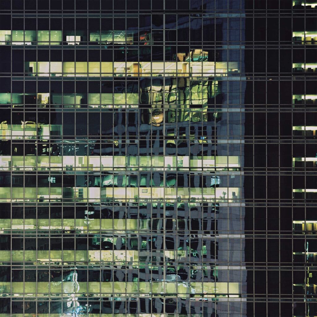 Night reflections: An office building in Seoul illuminated from within, with interior lights blending seamlessly with exterior reflections on its massive glass architecture, creating captivating organic textures