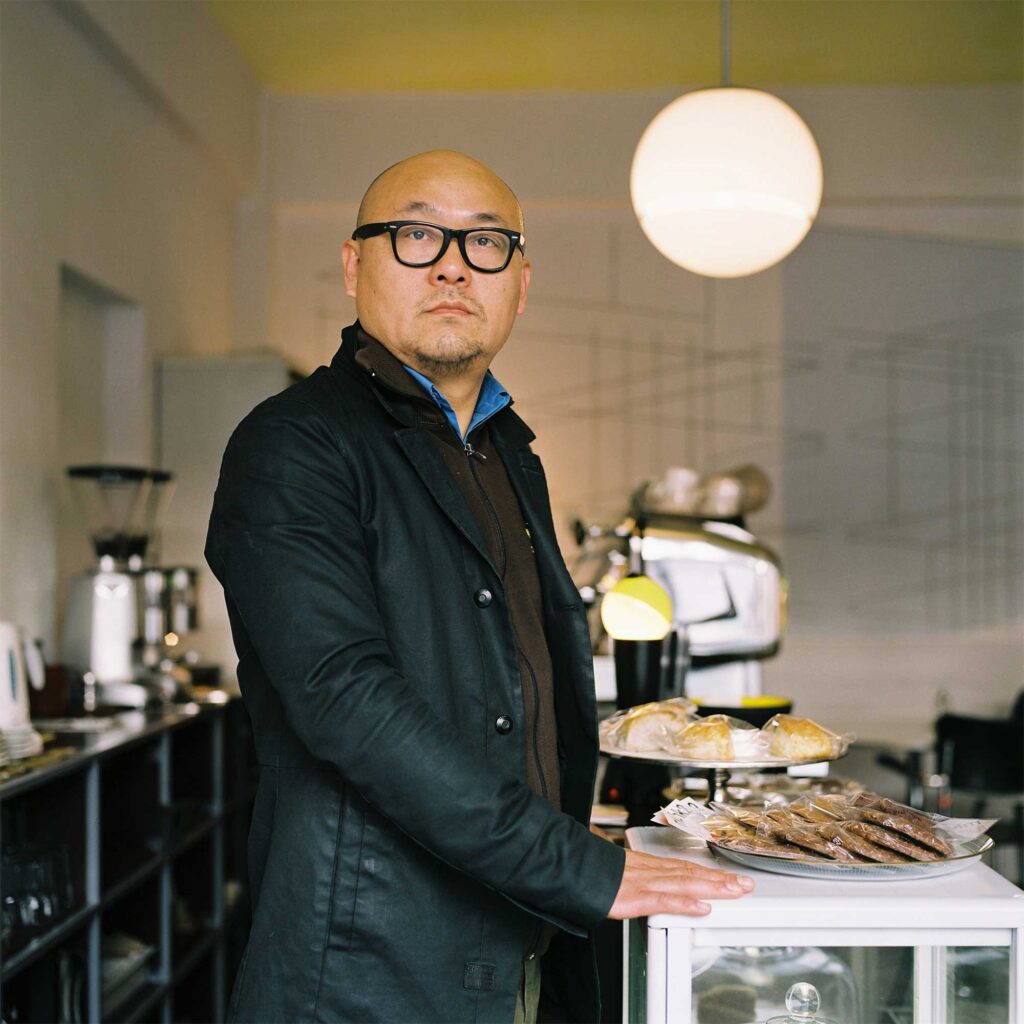 A portrait of a cafe owner in Seoul, South Korea, standing at the coffee counter and looking into the camera