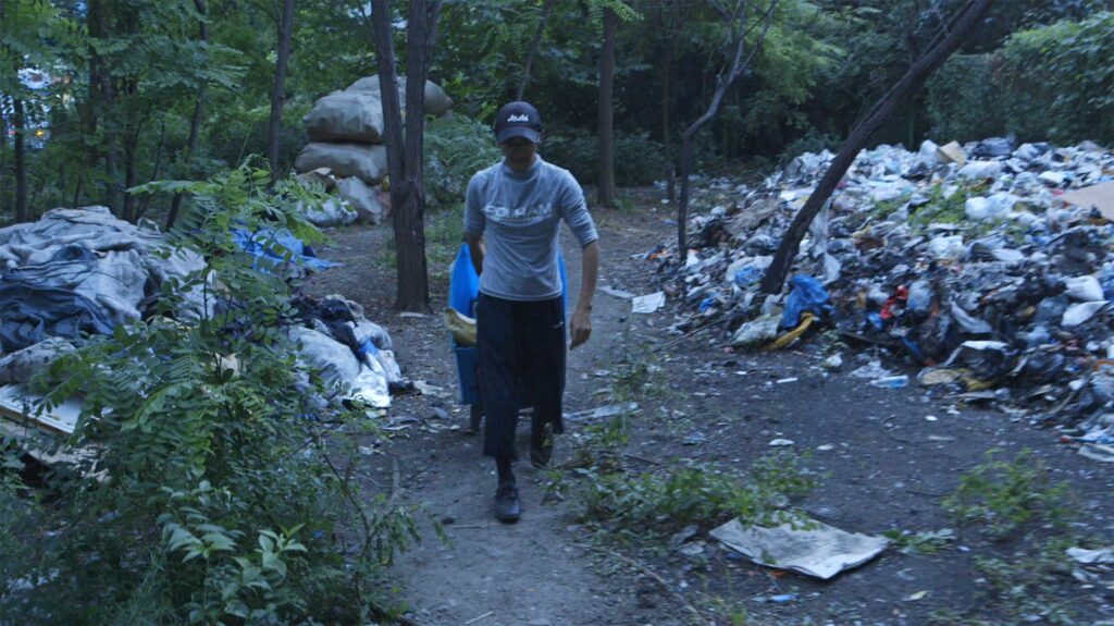 A screenshot from the Varúð music video by Icelandic band Sigur Rós, depicting a homeless man as he takes off, pulling his cart from the small park where he camps out into the night of Seoul, South Korea, to collect recyclables