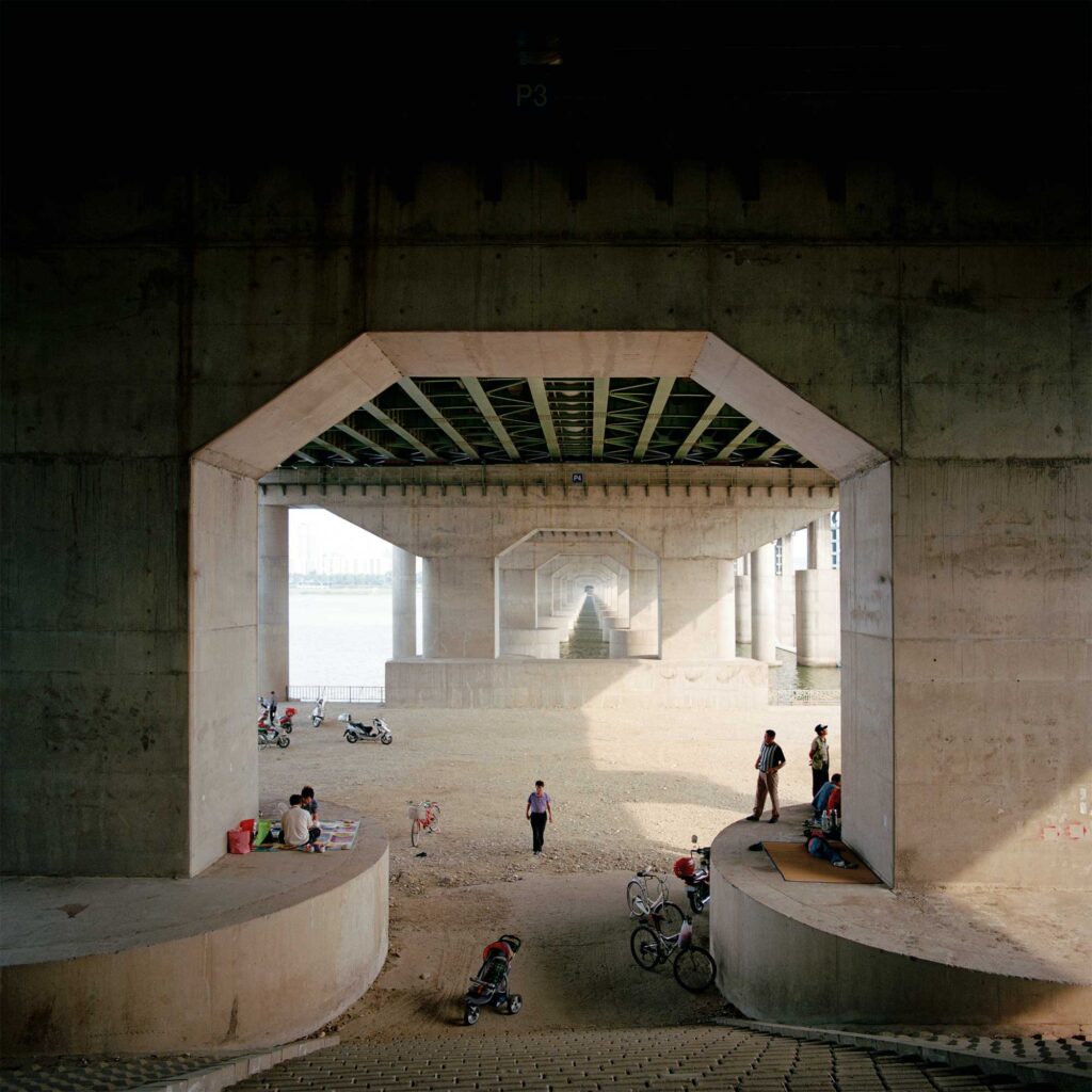 Individuals seeking shade on a scorching summer day under a bridge spanning the Han River in Seoul, South Korea
