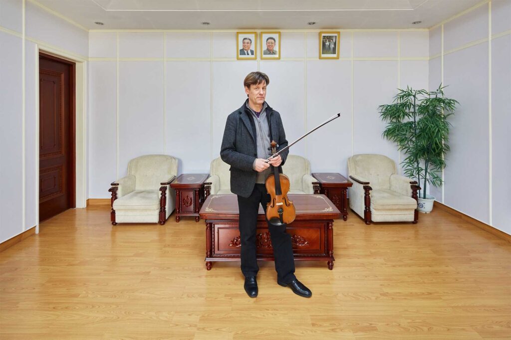 Munich Chamber Orchestra violinist in Pyongyang, North Korea, with portraits of North Korean leaders Kim Il-Sung and Kim Jong-Il on the wall