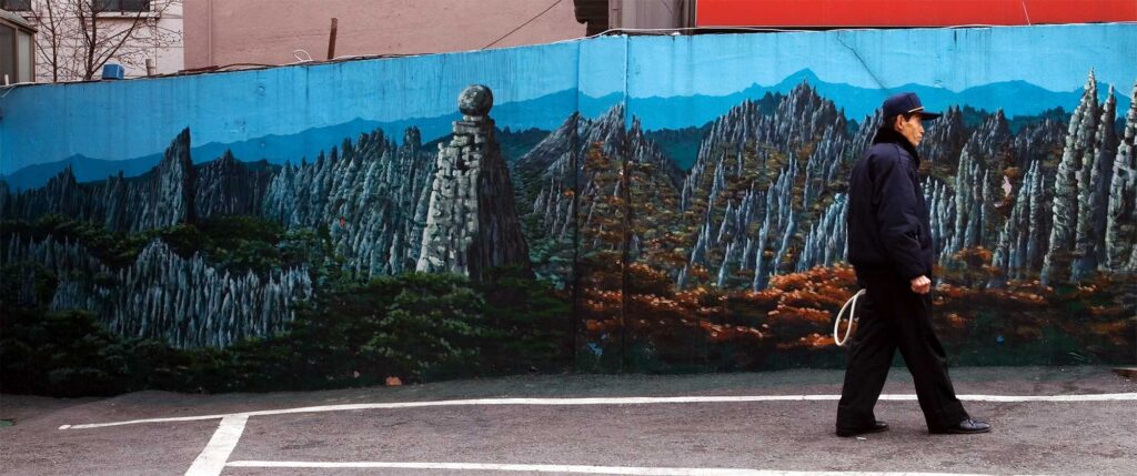 Urban mural depicting rocky Korean mountain landscape, with an older Korean man in parking instructor uniform