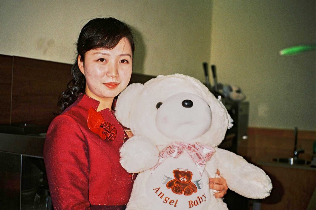 A woman dressed in red in Pyongyang, North Korea, holds up a large white teddy bear with 'Angel Baby' written on its belly.