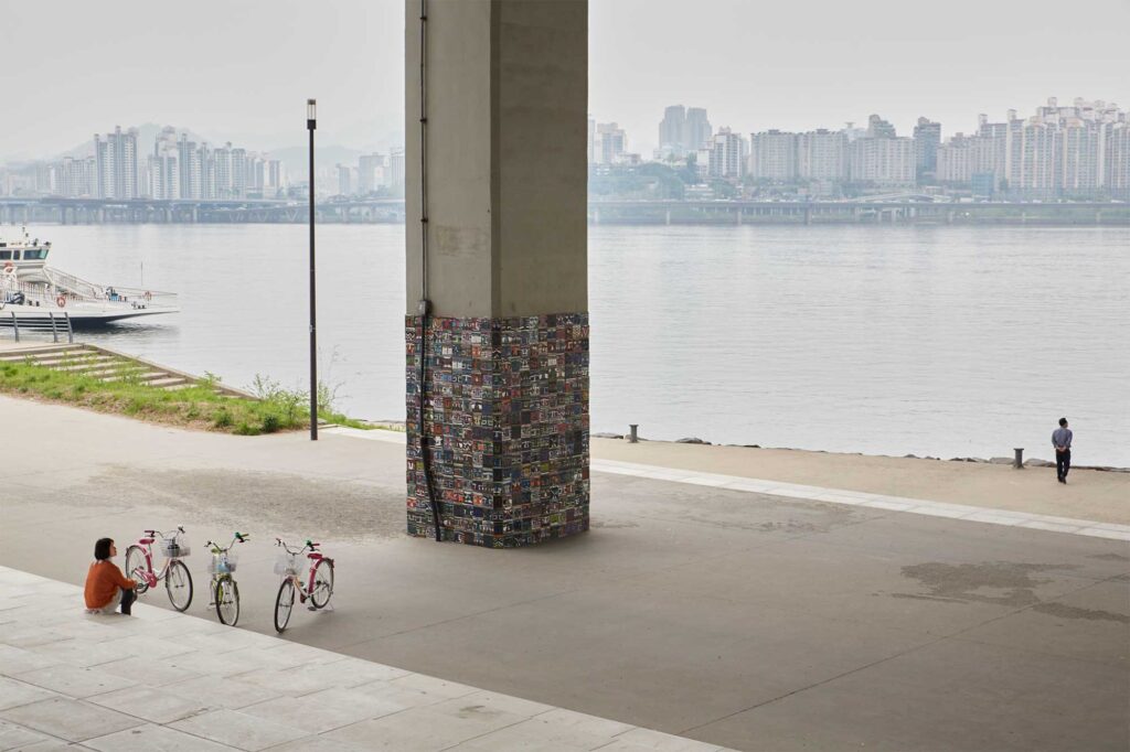 A woman takes a break from a bicycle ride on the staircase of the Han River bank in Seoul underneath a bridge, as a man walks up to the edge of the river bank