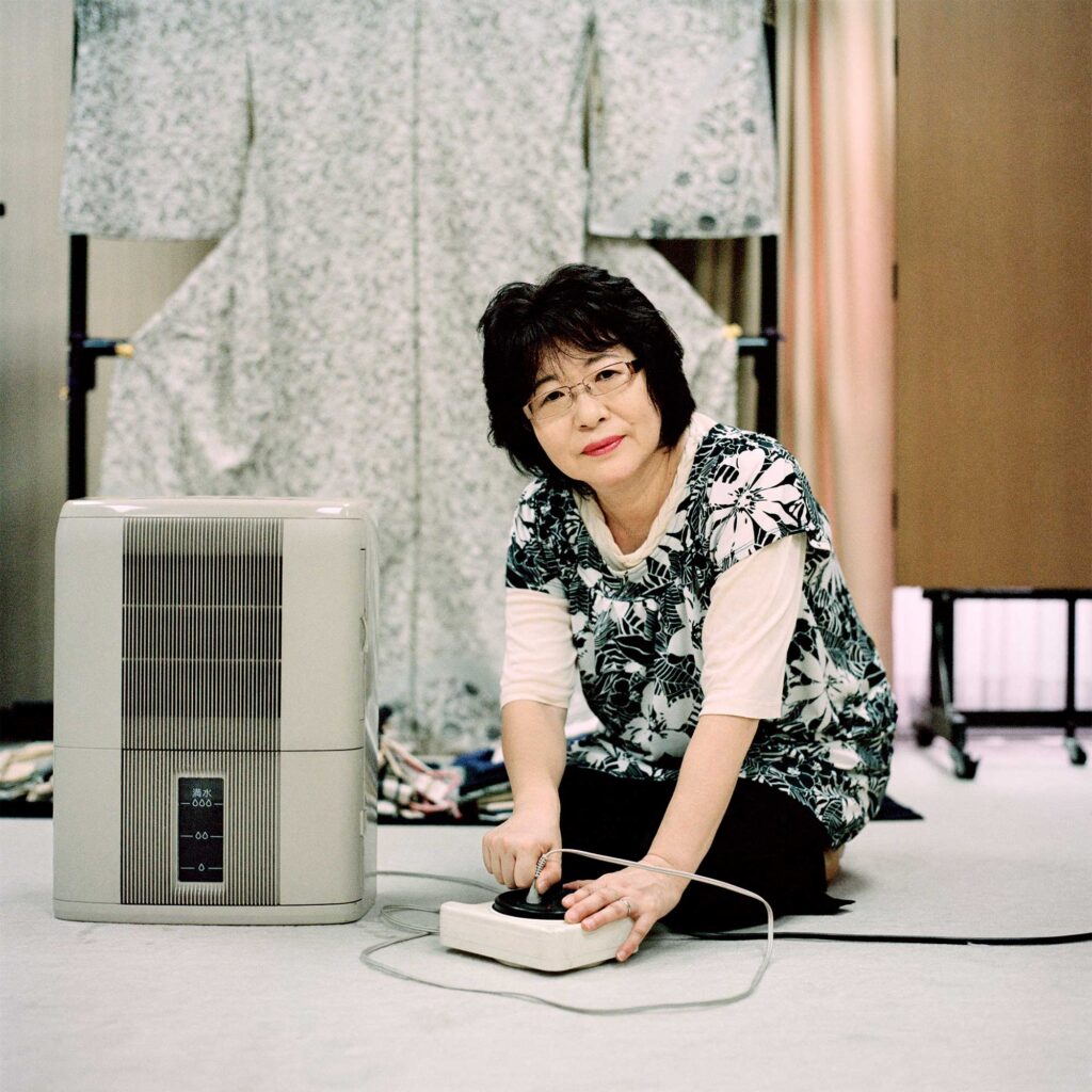 Elderly female tailor in Tokyo unplugging small fan, conserving energy post-Fukushima