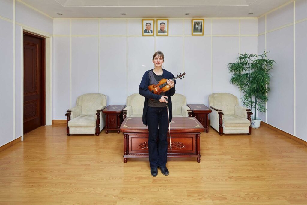 Munich Chamber Orchestra violinist in Pyongyang, North Korea, with portraits of North Korean leaders Kim Il-Sung and Kim Jong-Il on the wall