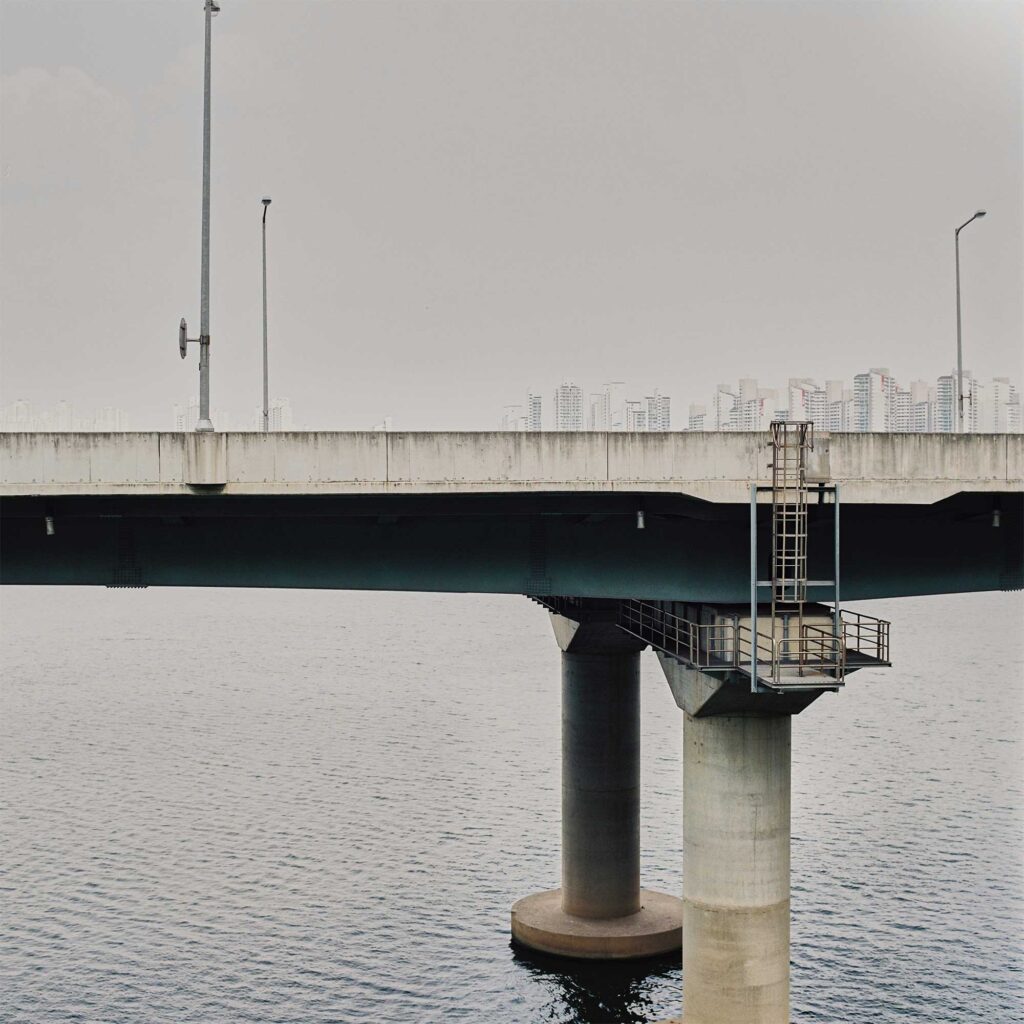 The Olympic Express Highway towers over the Han River in Seoul, South Korea. Apartment buildings in the background create an optical illusion, seemingly piling up on the highway itself
