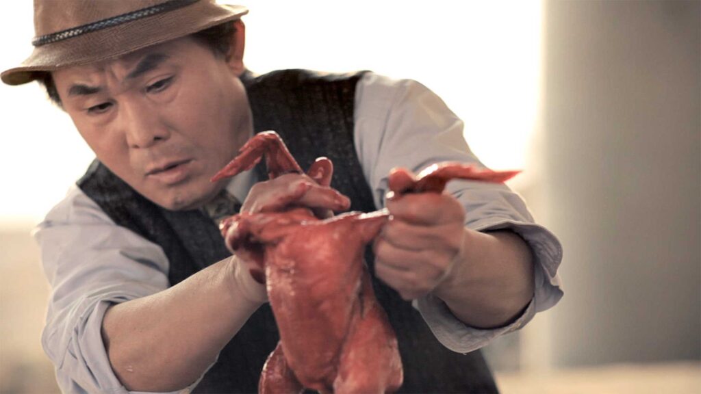 A scene from Röyksopp's 'Senior Living' music video: An older man gives birth to a chicken during a picnic beneath a flyover highway bridge near the Han River in Seoul, South Korea.