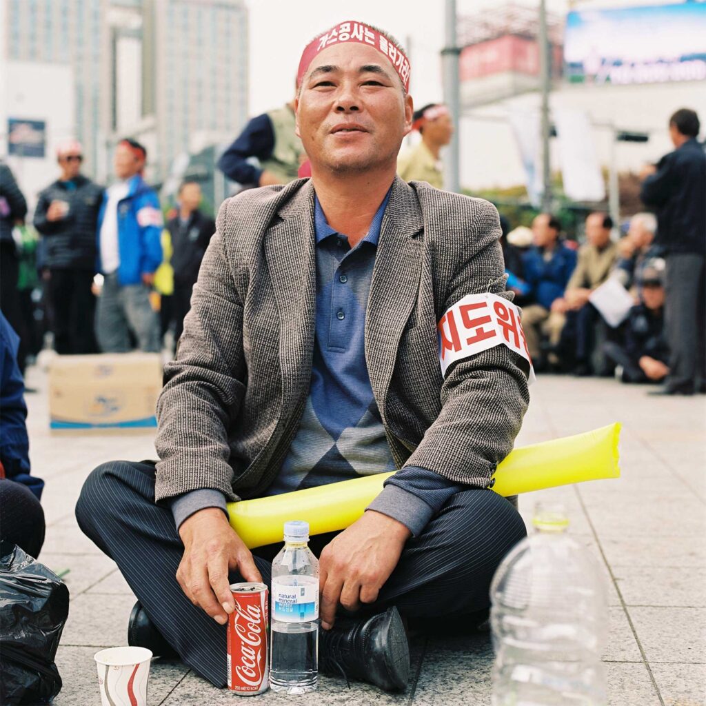 A Korean man sits on the street during a protest in Gwanghwamun area, Seoul, with a bottle of water and a Coke beside him
