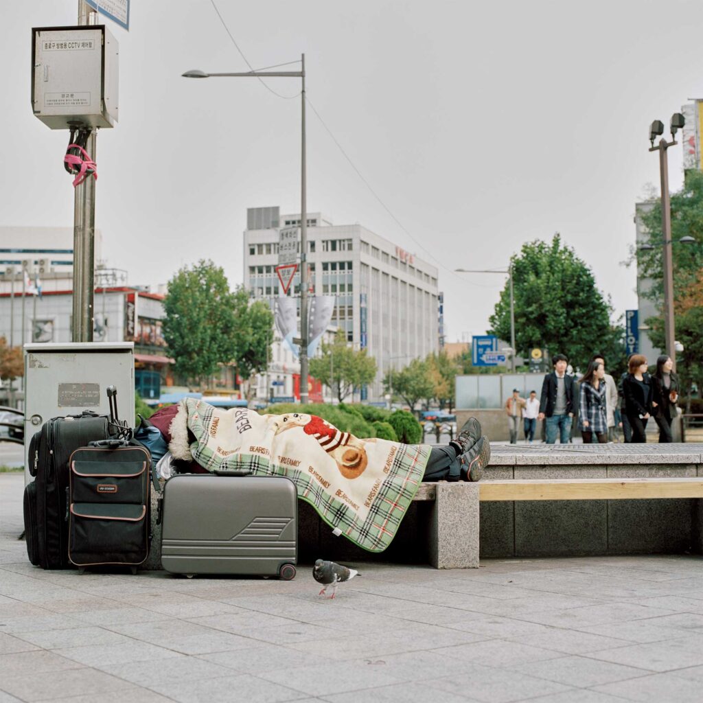 A homeless person, covered by a blanket, rests on a bench with belongings nearby in Jongro district, Seoul, South Korea