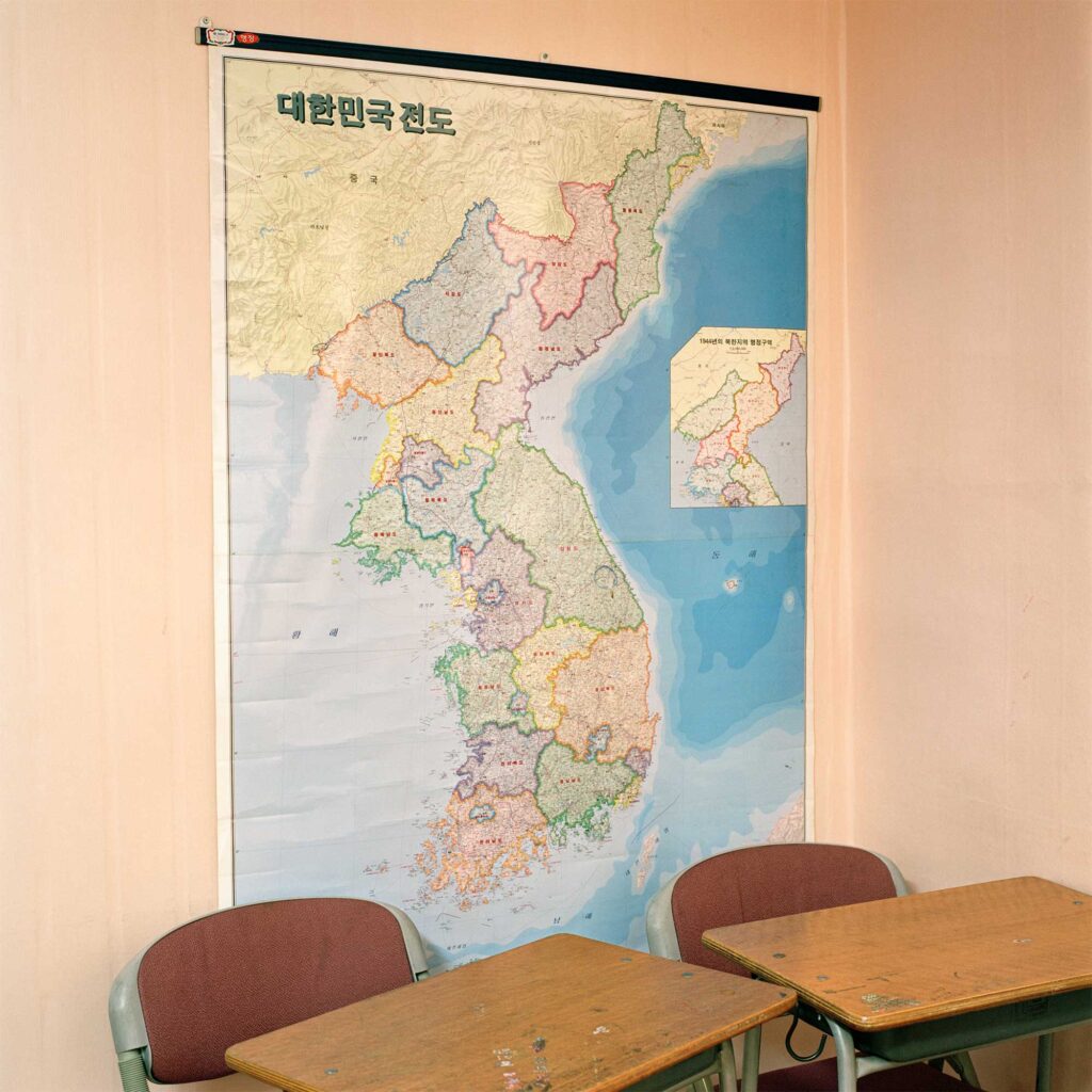A large map on a classroom wall depicts the Korean Peninsula without a border dividing North Korea from South Korea