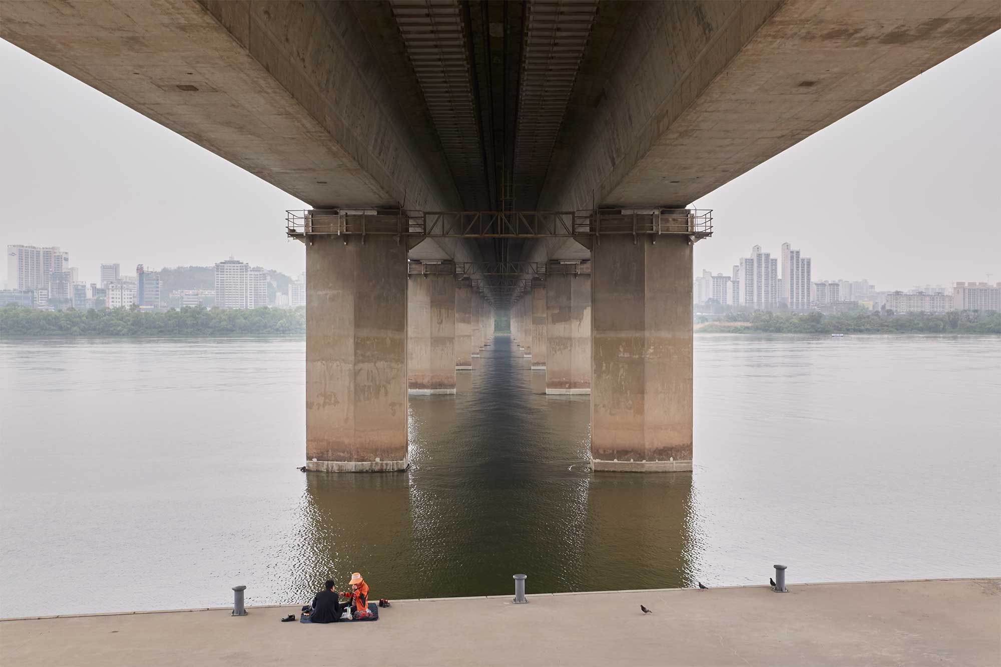 Two people take a rest underneath a bridge at the bank of Han River in Seoul, South Korea