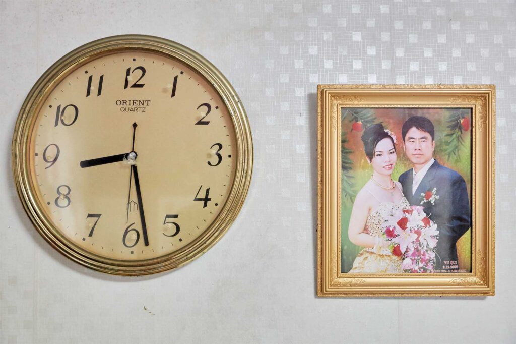 The Vietnamese wedding photo of a Korean-Vietnamese couple, framed and hanging next to a round clock on the wall of the couple's bedroom.